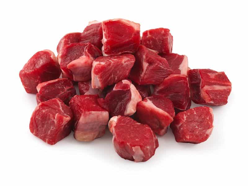 Cubos de carne de res cruda apilados sobre fondo blanco