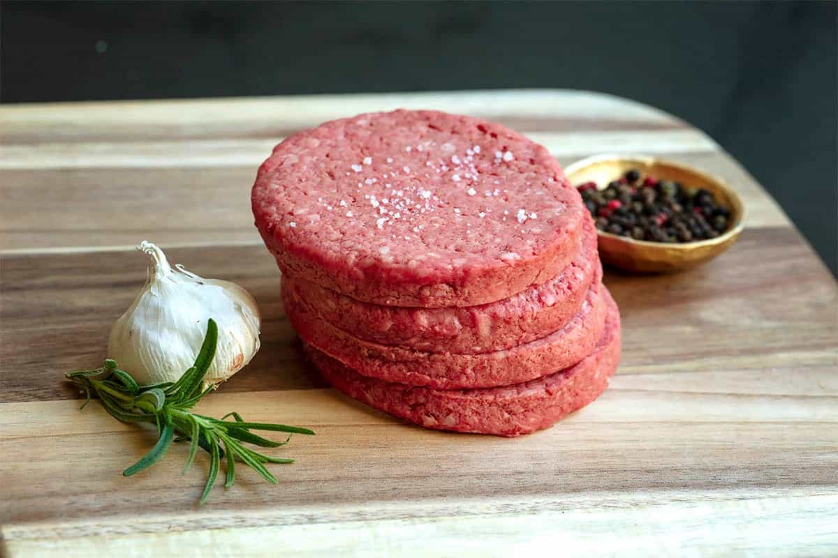 Hamburguesas de res crudas apiladas sobre una tabla de cortar