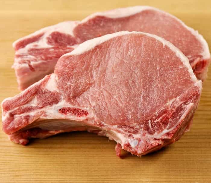 Chuletas de cerdo crudas con hueso sobre una tabla de madera