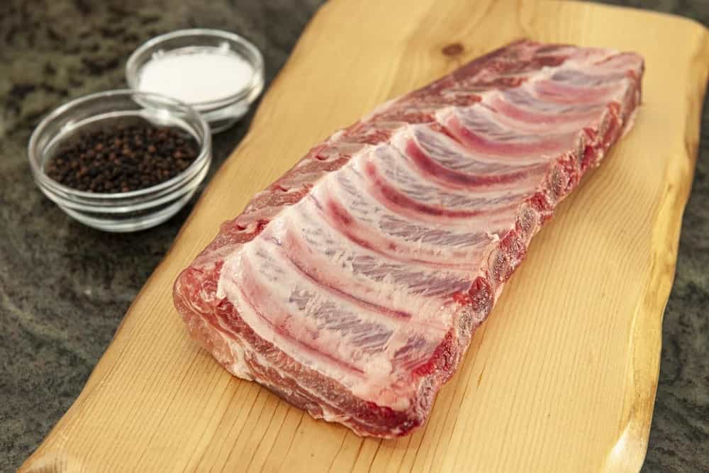 Costillar de cerdo crudo con granos de pimienta sobre una tabla de madera
