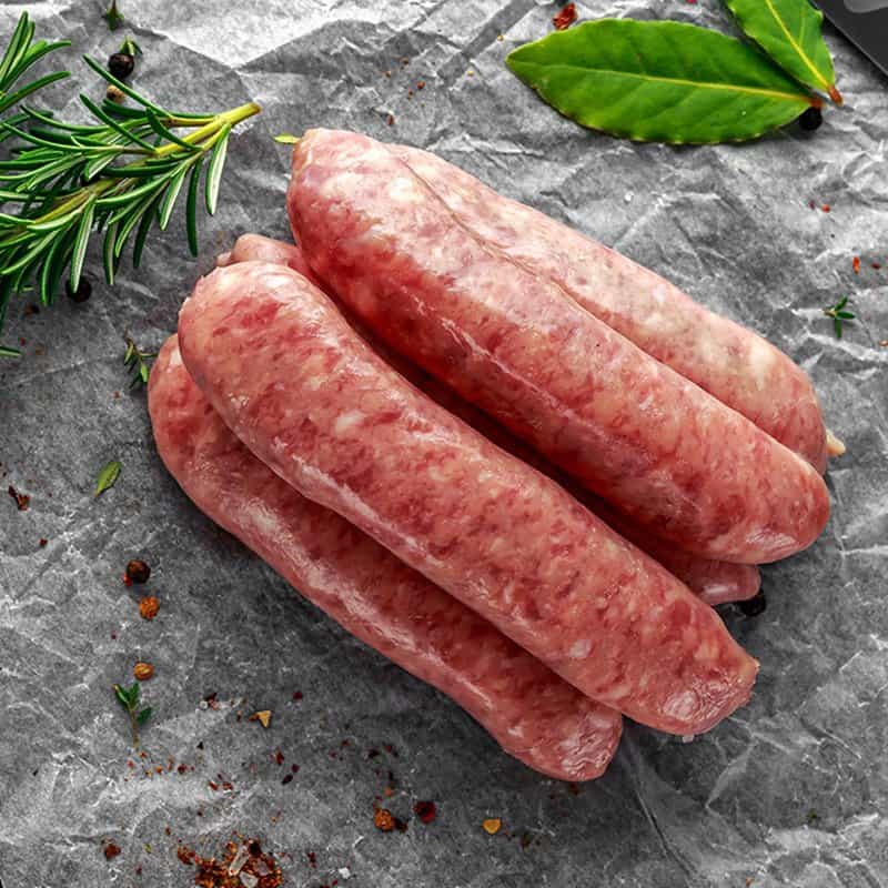 Salchichas crudas dispuestas sobre papel de horno con hierbas