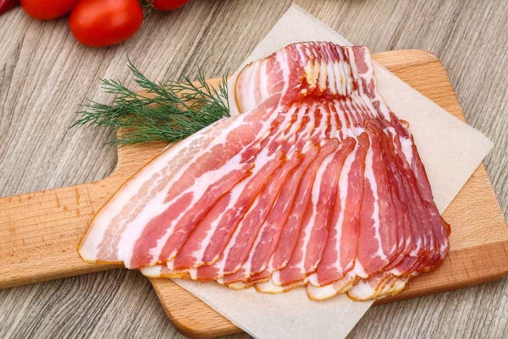 Tocineta cruda en lonjas sobre una tabla de cortar