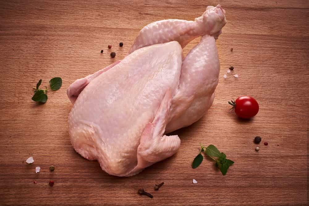 Pollo entero crudo sobre una tabla de madera con hierbas