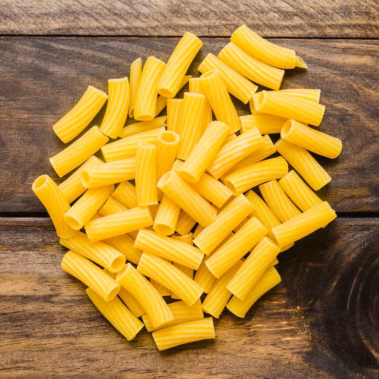 Montón de pasta corta en tubos estriados sobre una mesa de madera